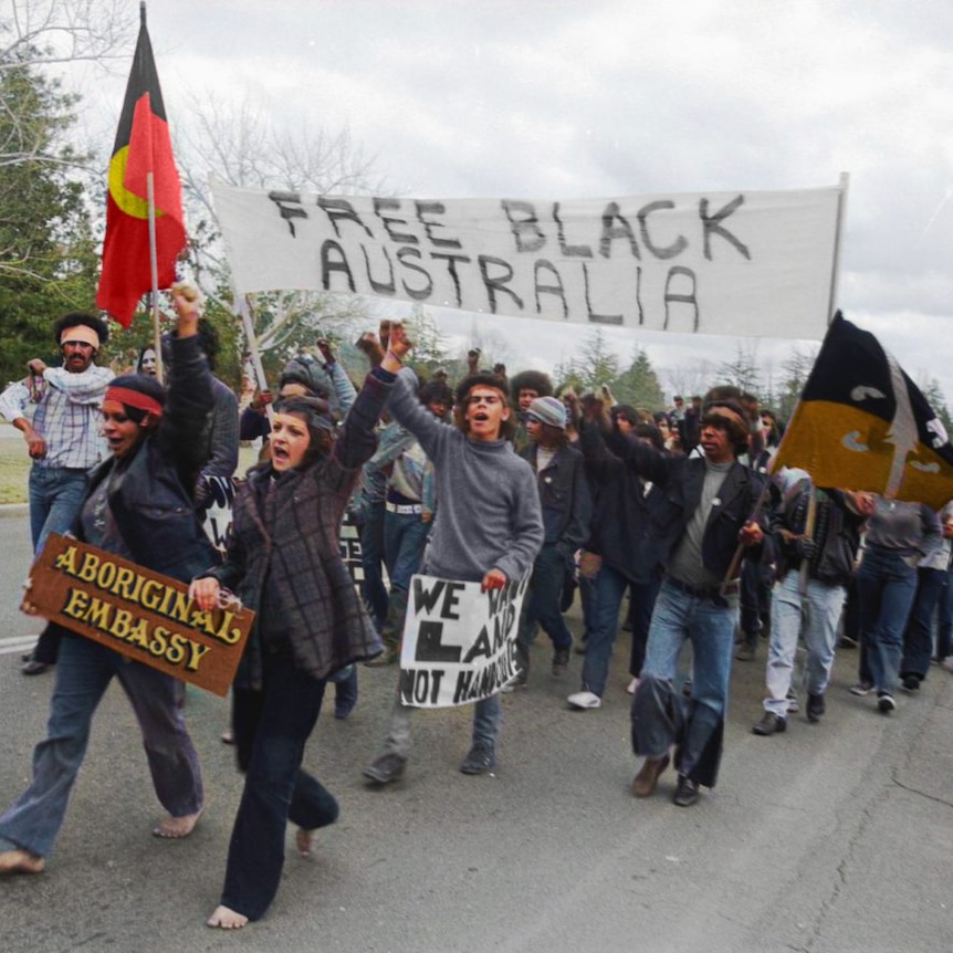 People marching and holding up the Aboriginal flag and a sign saying free black Australia