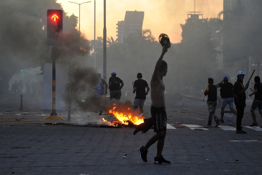 A person stands on a street in Bolivia with a small fire burning under a hazy, smoky sky.