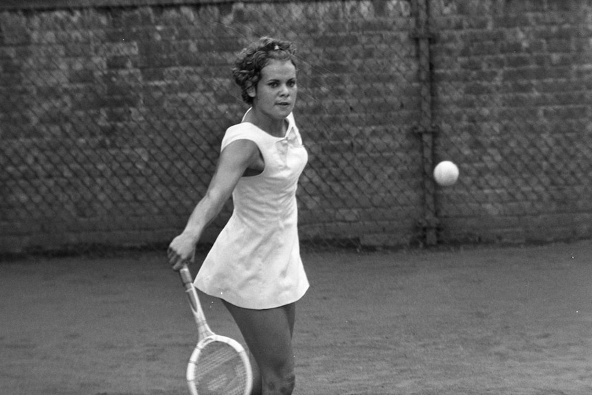 A black and white photo of a young woman staring at a tennis ball that she is about to hit.