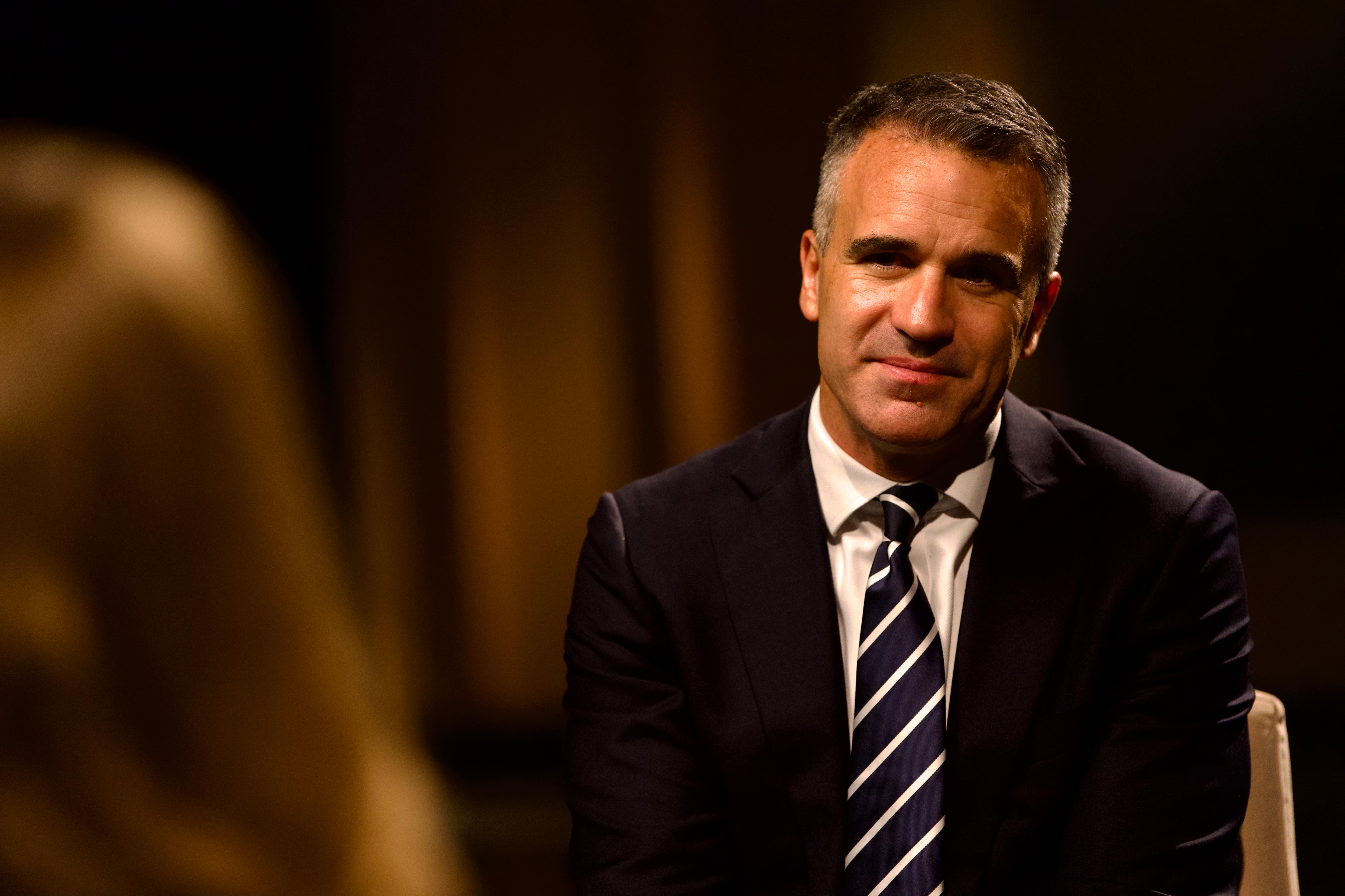 Peter Malinauskas in a suit sitting opposite a reporter in a dark room