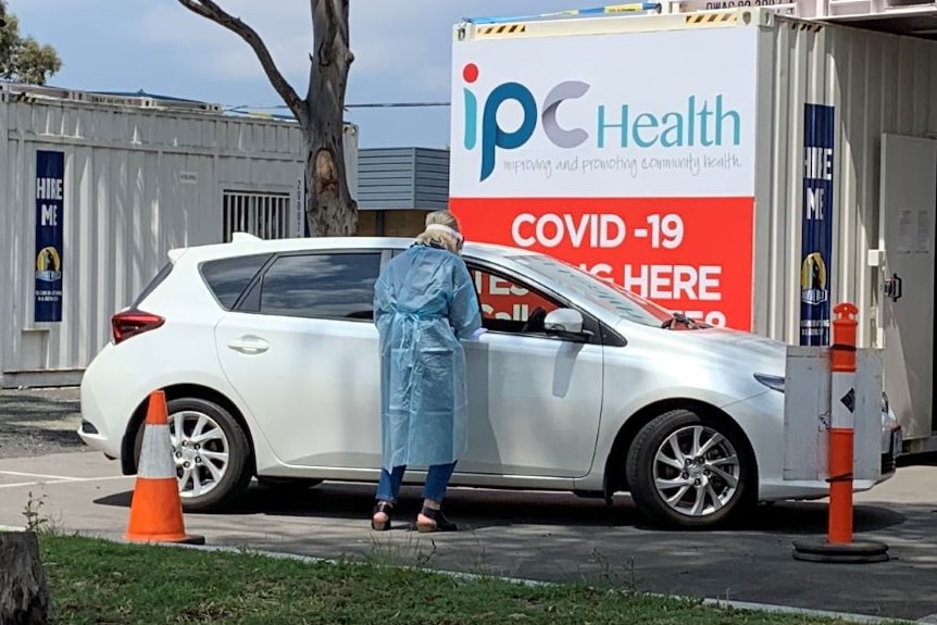 A woman in PPE stands at the window of a car which has driven up to a coronavirus testing site.