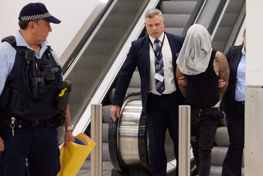 police hold onto a man who has been arrested and is wearing a head covering