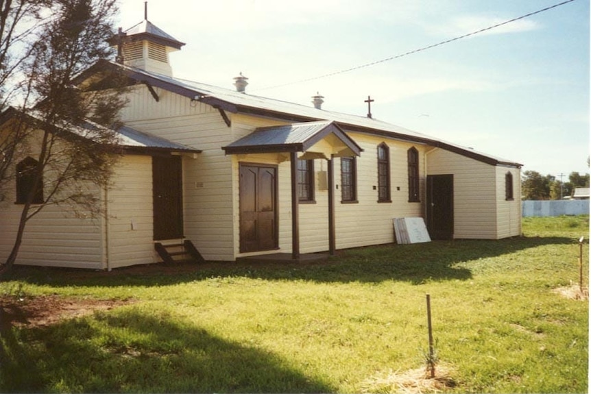 White weatherboard building with brown facades and cross.