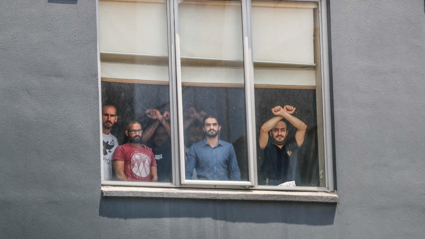Six men are pictured in the window of the grey Mantra Hotel in Preston, some have their arms up and wrists crossed in an X.