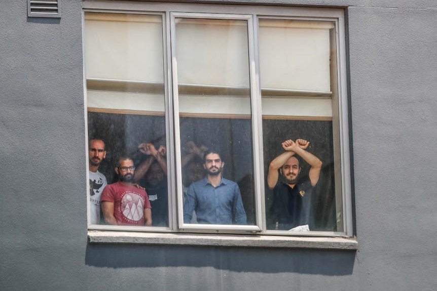 Six men are pictured in the window of the grey Mantra Hotel in Preston, some have their arms up and wrists crossed in an X.