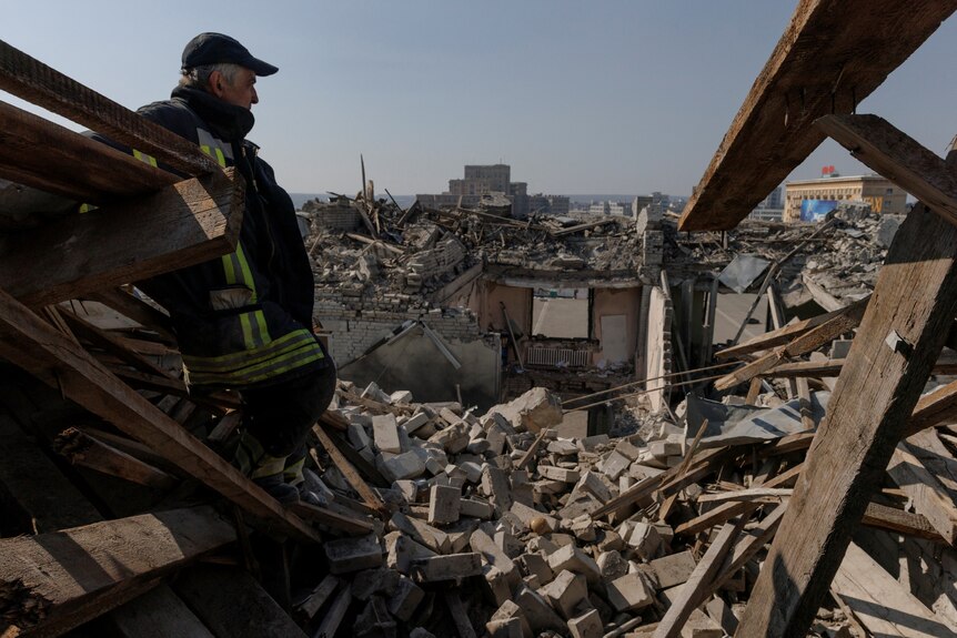 Man stands amidst rubble on a rooftop that was hit by shelling.