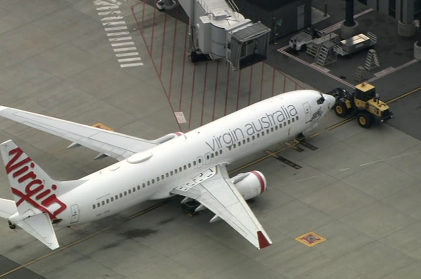 A front-end loader sits in front of a Virgin Australia plane.