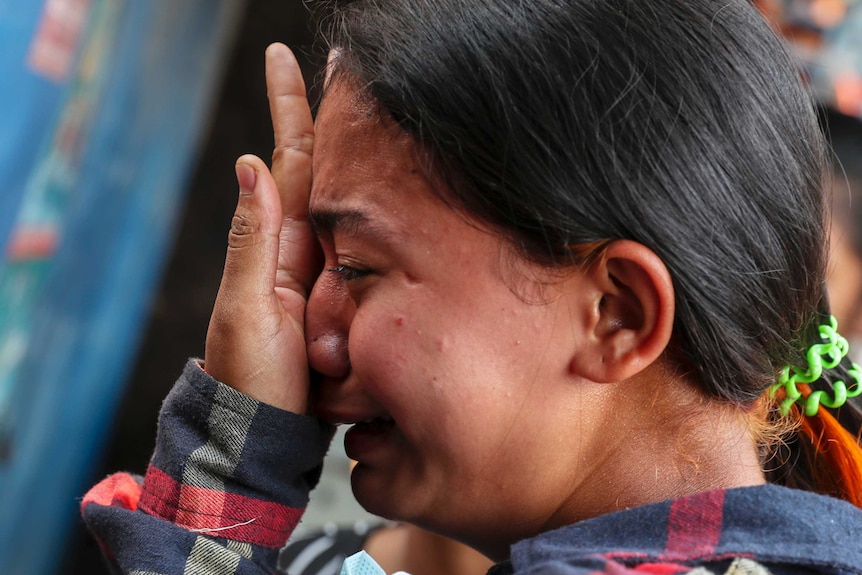 A close up photo shows a crying woman pressing her open left palm on her nose.