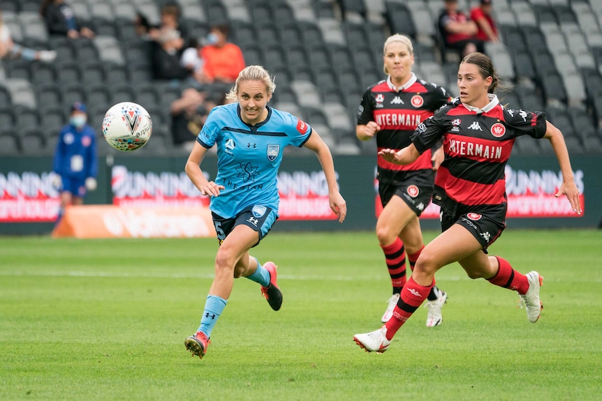 Mackenzie Hawkesby in the blue kit of Sydney FC is chased by Olivia Price in the red and horizontal black stripes of WSW