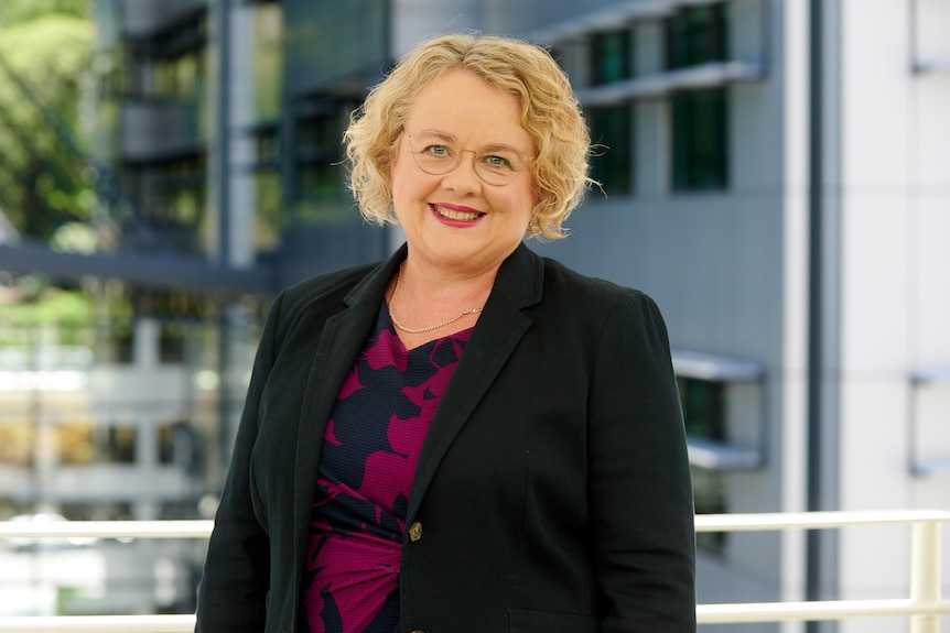 Elizabeth Shearer stands on a balcony smiling while wearing a smart black jacket. 