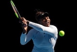 Serena Williams wears a white long-sleeve shirt and black visor as she leans in to hit tennis ball with racket in her hands.