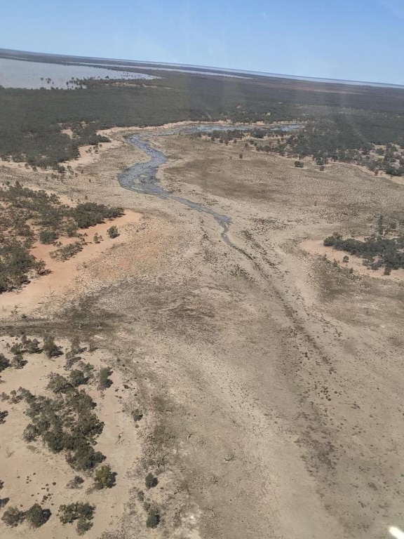 An aerial view of water flowing into parched lake bed.