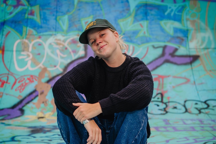 A young woman sits smiling on a skateboard.