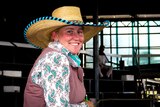 A woman wearing a straw hat stands smiling at the camera in a cattle sale yard