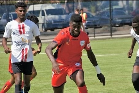 Two footballers in white jerseys close in on one in a red jersey