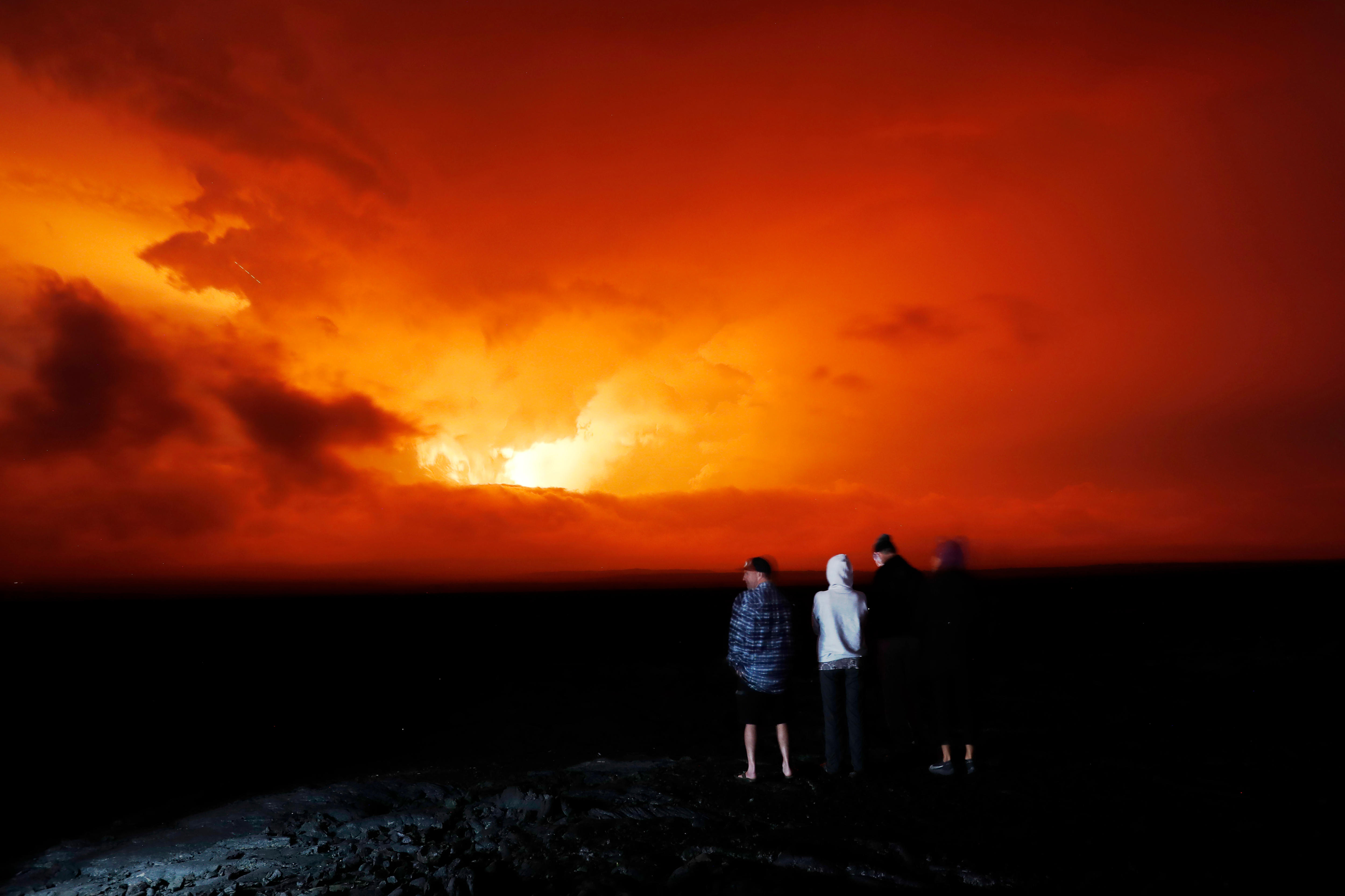 A group of people watch the eruption of a volcano light up the night sky
