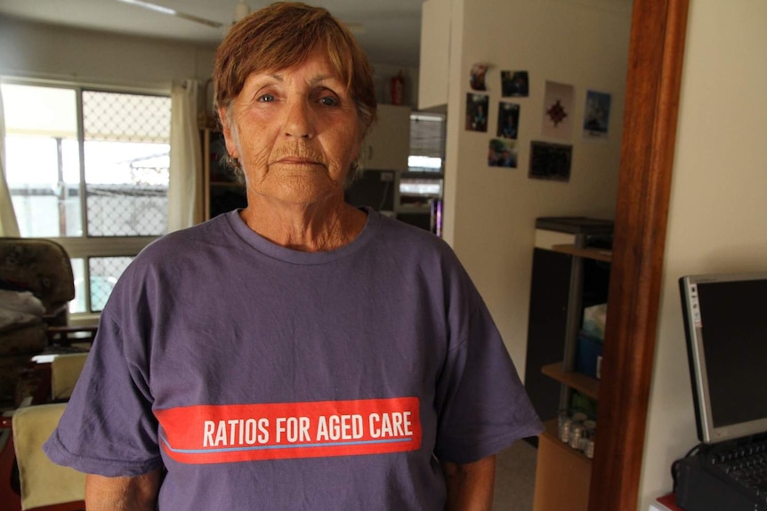 A woman wearing a purple shirt with red writing that says 'ratios for aged care' stands front on looking at the camera
