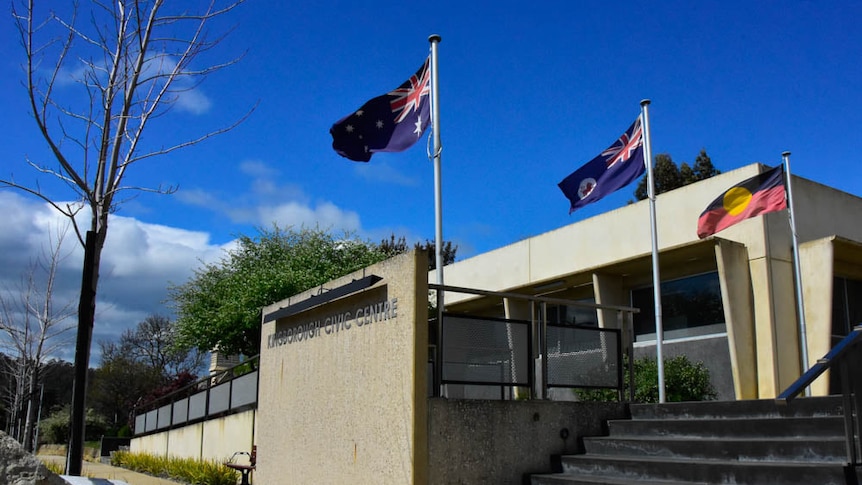 The Australian, Tasmanian and Aboriginal flags flying outside a single-story public building.