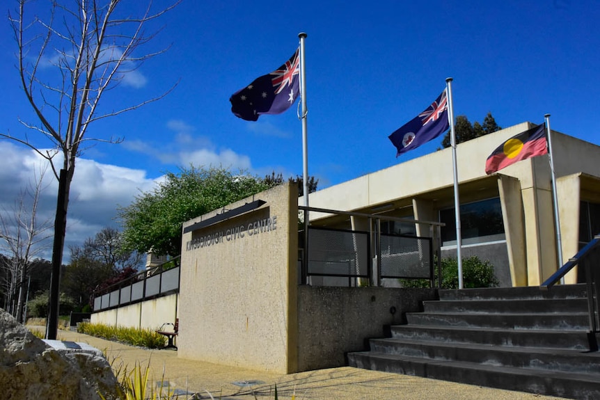 The Australian, Tasmanian and Aboriginal flags flying outside a single-story public building.