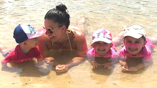 Hannah Baxter with her children at the beach, laying down in the water with her three children.