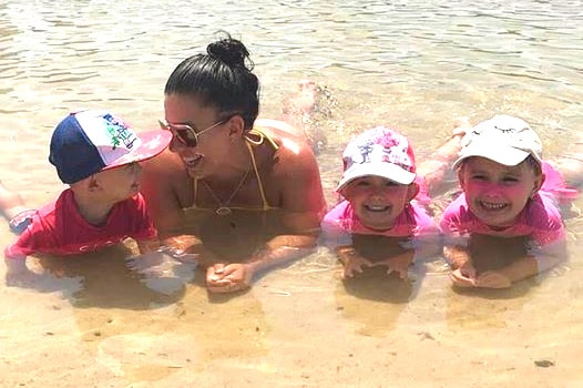 Hannah Baxter at the beach, laying down in the water with her three children.