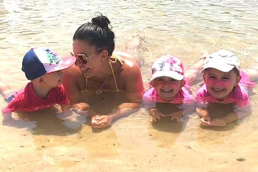 Hannah Baxter with her children at the beach, laying down in the water with her three children.