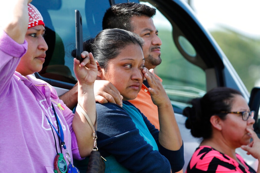 A clsoe up photo shows a woman wiping away a tear as she stands among a crowd.