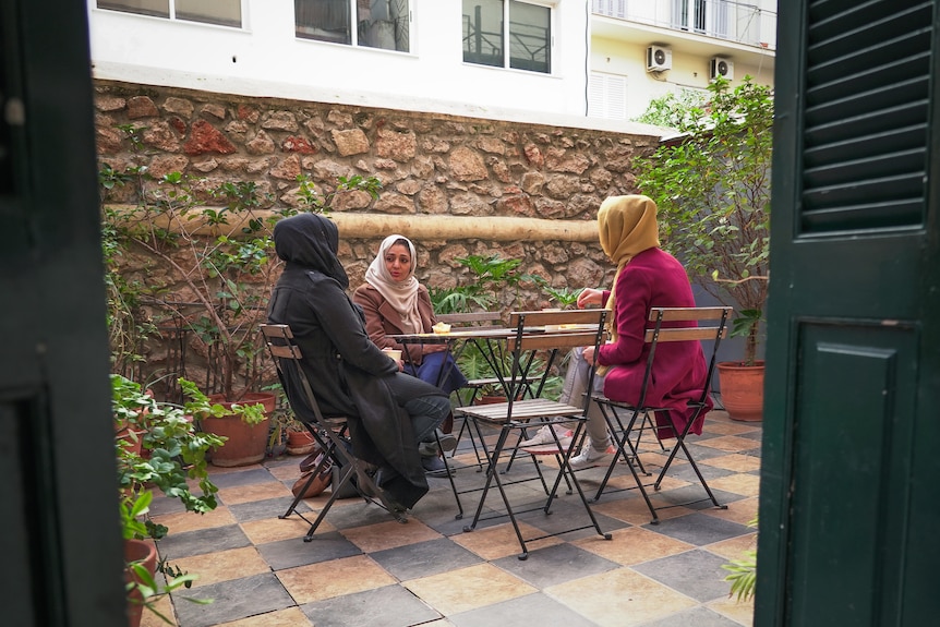 Three women wearing hajibs sit around a table outside.