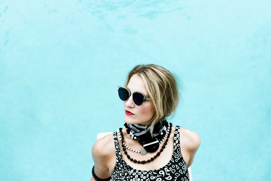 Glamourous women sits by the pool with sunglasses to depict creative style.