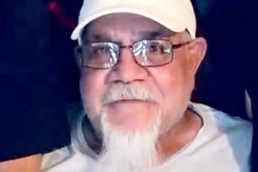 an elderly man wearing glasses and a cap and looking