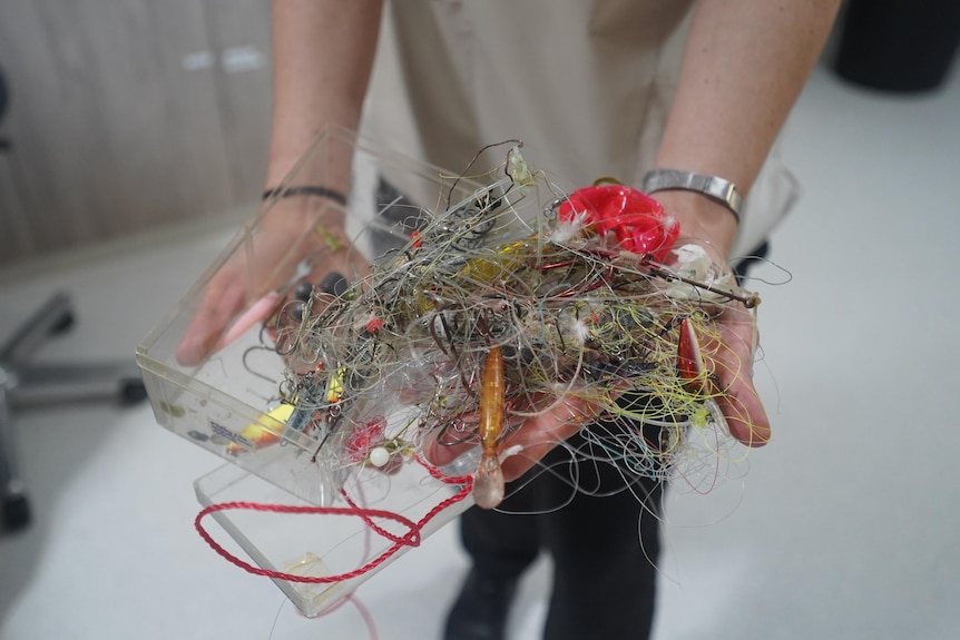 A woman holds a tangled web of fishing lines and hooks