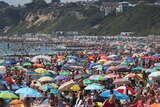 Thousands of people with colourful umbrellas pack a beach beneath cliffs.