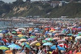 Thousands of people with colourful umbrellas pack a beach beneath cliffs.