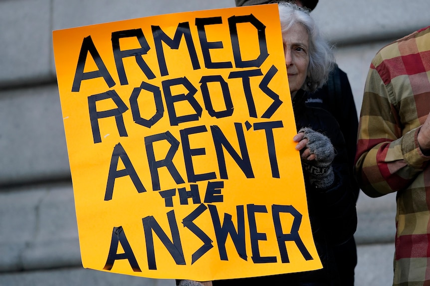 A woman holds a bright yellow sign that says, 'armed robots aren't the answer' 
