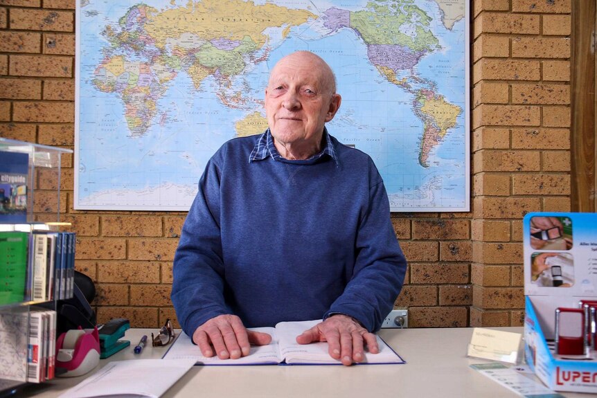 Ian Morton sits at a desk with a large world map behind him.