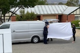Police hold a white sheet in front of a suburban home.