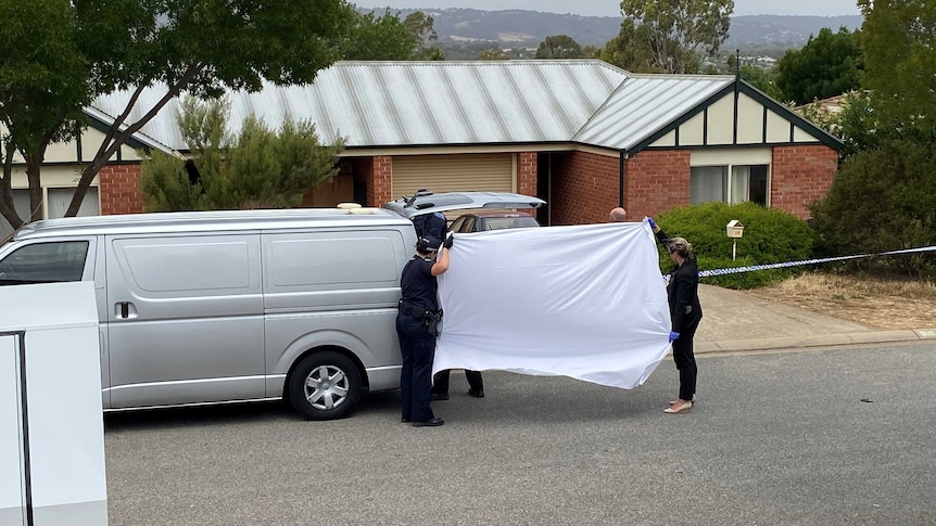 Police hold a white sheet in front of a suburban home.