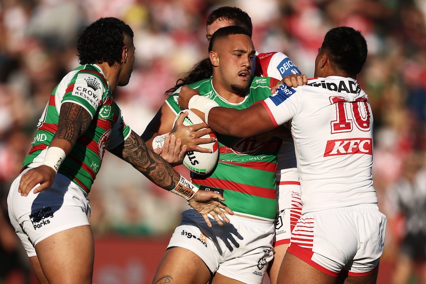A South Sydney NRL player holds the ball as he is tackled by a St George Illawarra opponent.