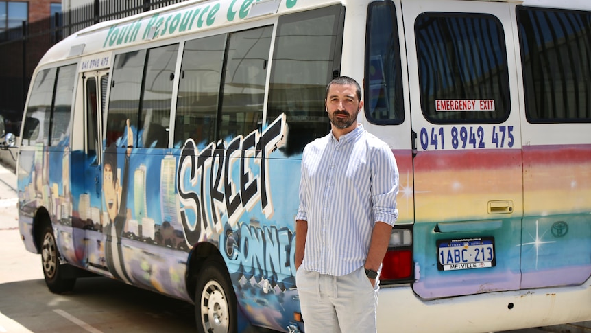 A man in shorts and a shirt stands in front of a busy emblazoned with street art and the words Street Connect 