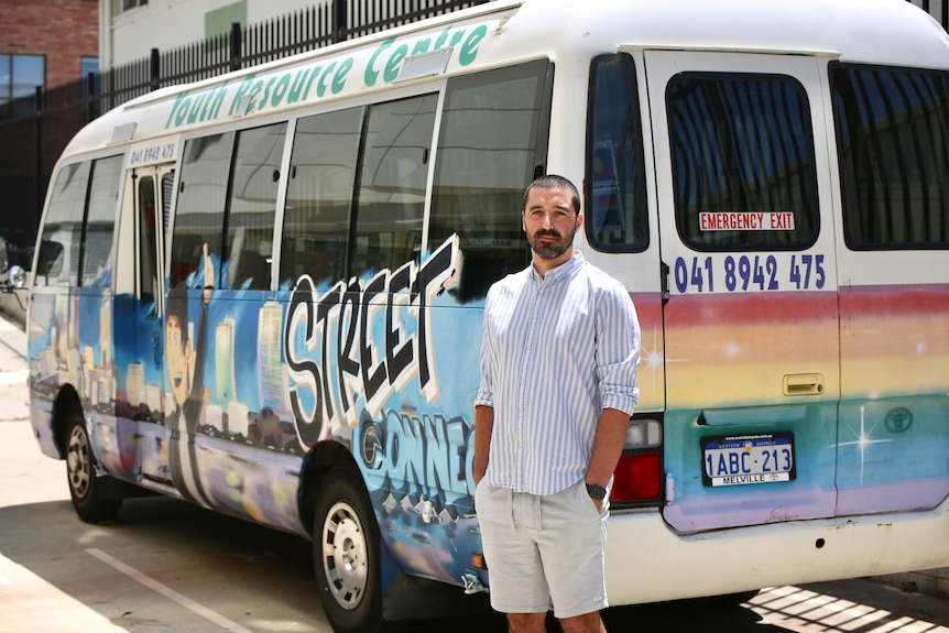 A man in shorts and a shirt stands in front of a busy emblazoned with street art and the words Street Connect 