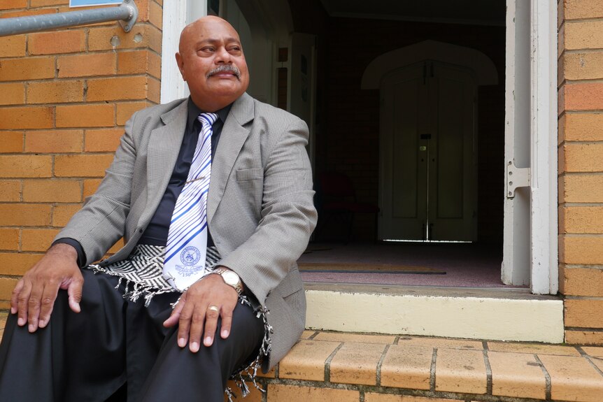 Mele Ngauamo sitting outside a tan brick building, looking to the right. 