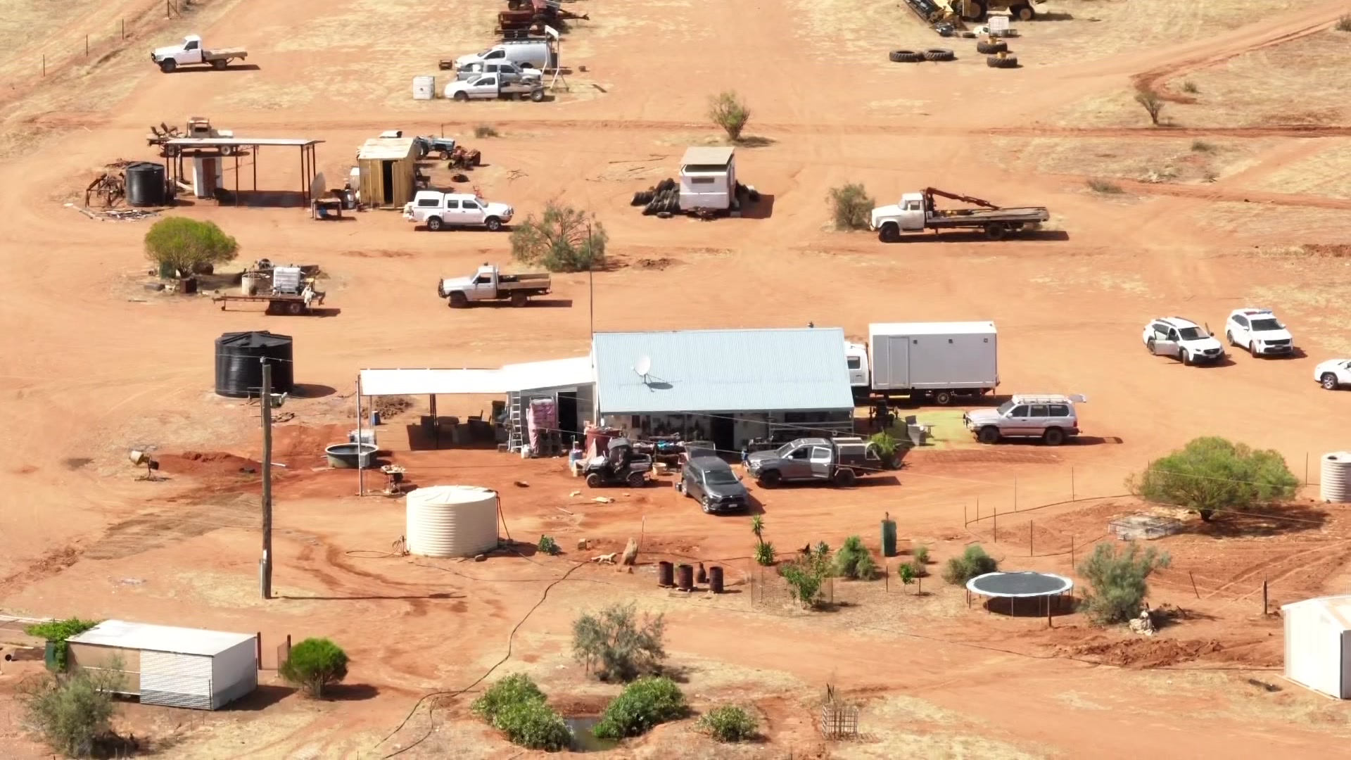 Vista aérea de um prédio em terra vermelha, com carros espalhados ao redor.