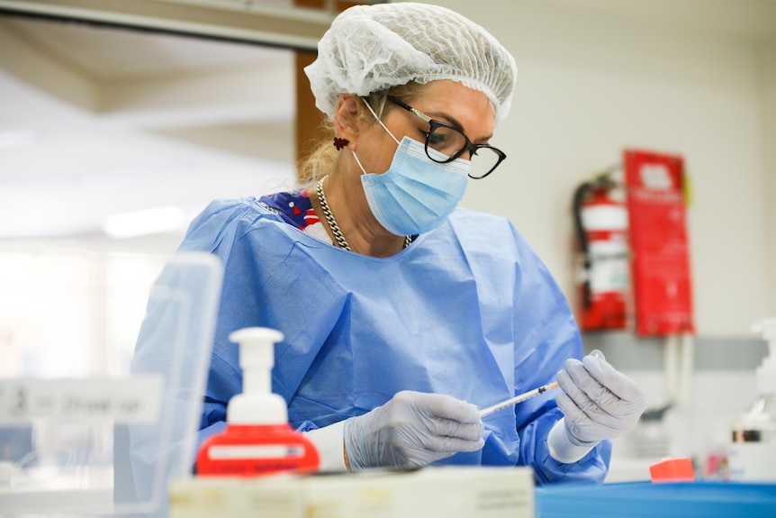 A nurse wearing PPE holding a needle and vial.