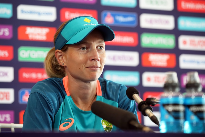 Australian cricket captain Meg Lanning sits at a desk with a bank of microphones in front of her at a press conference.