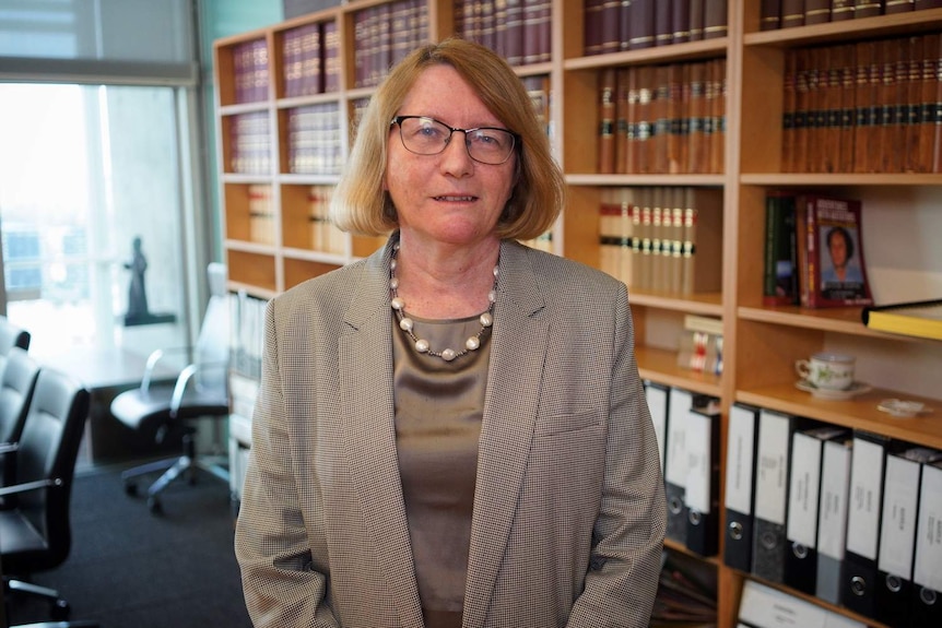 Chief Justice Catherine Holmes stands in an office with law books on shelves behind her.
