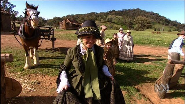 Woman in period costume stands in front of horse and cart