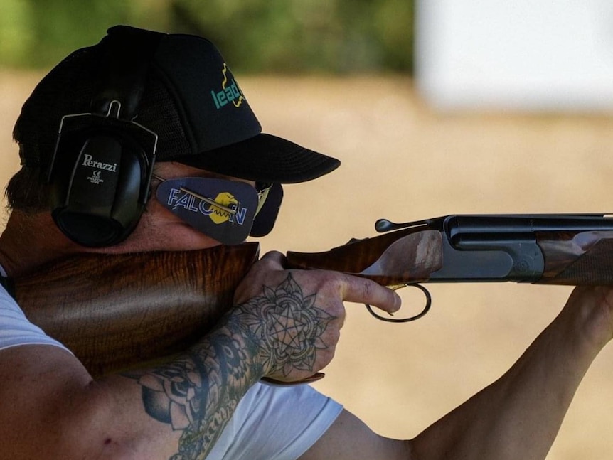A man wearing goggles and earmuffs looks down the sights of a shotgun to the right.