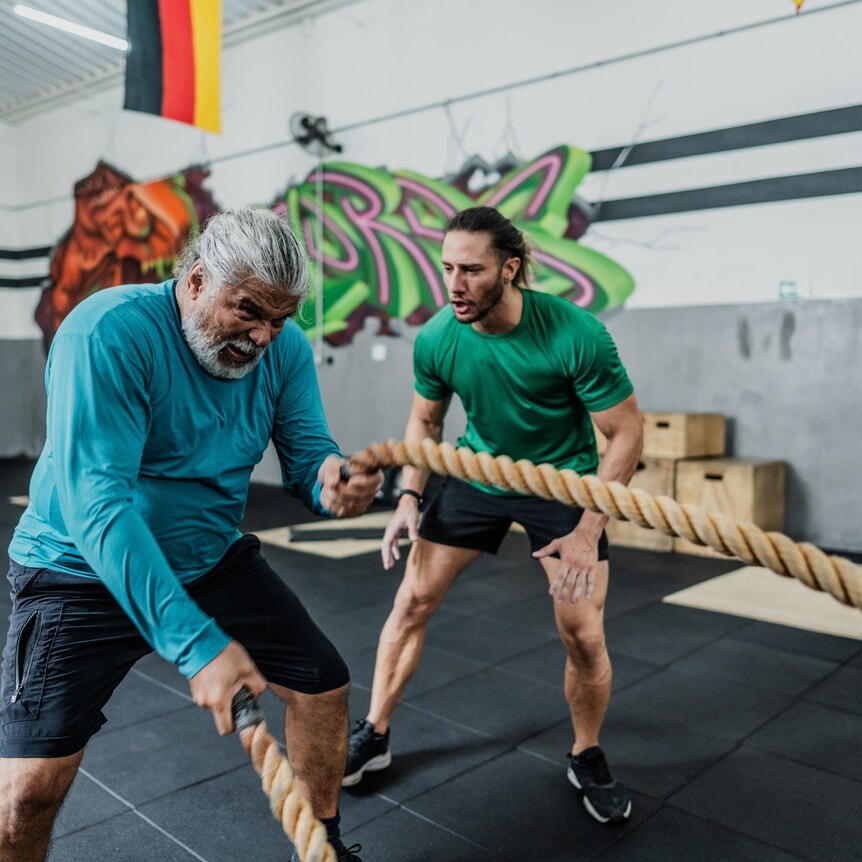 Man exercising with ropes and with his coach at the gym