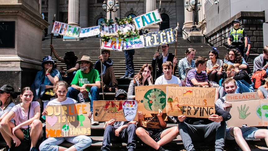 Climate change protesters sitting on the steps of the Victorian Parliament holding signs.