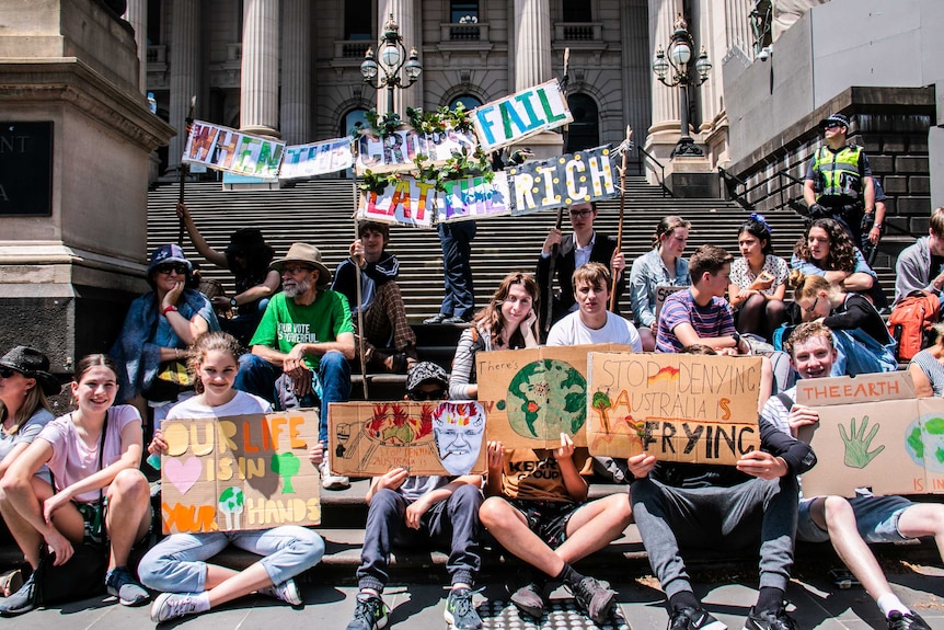Climate change protesters sitting on the steps of the Victorian Parliament holding signs.